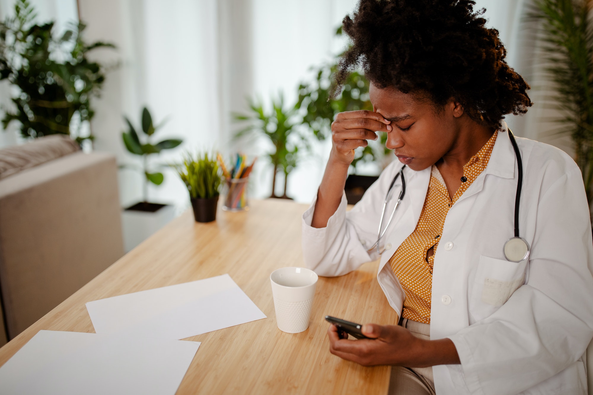 Closeup portrait sad unhappy health care professional with headache, stressed, sleepy holding phone.