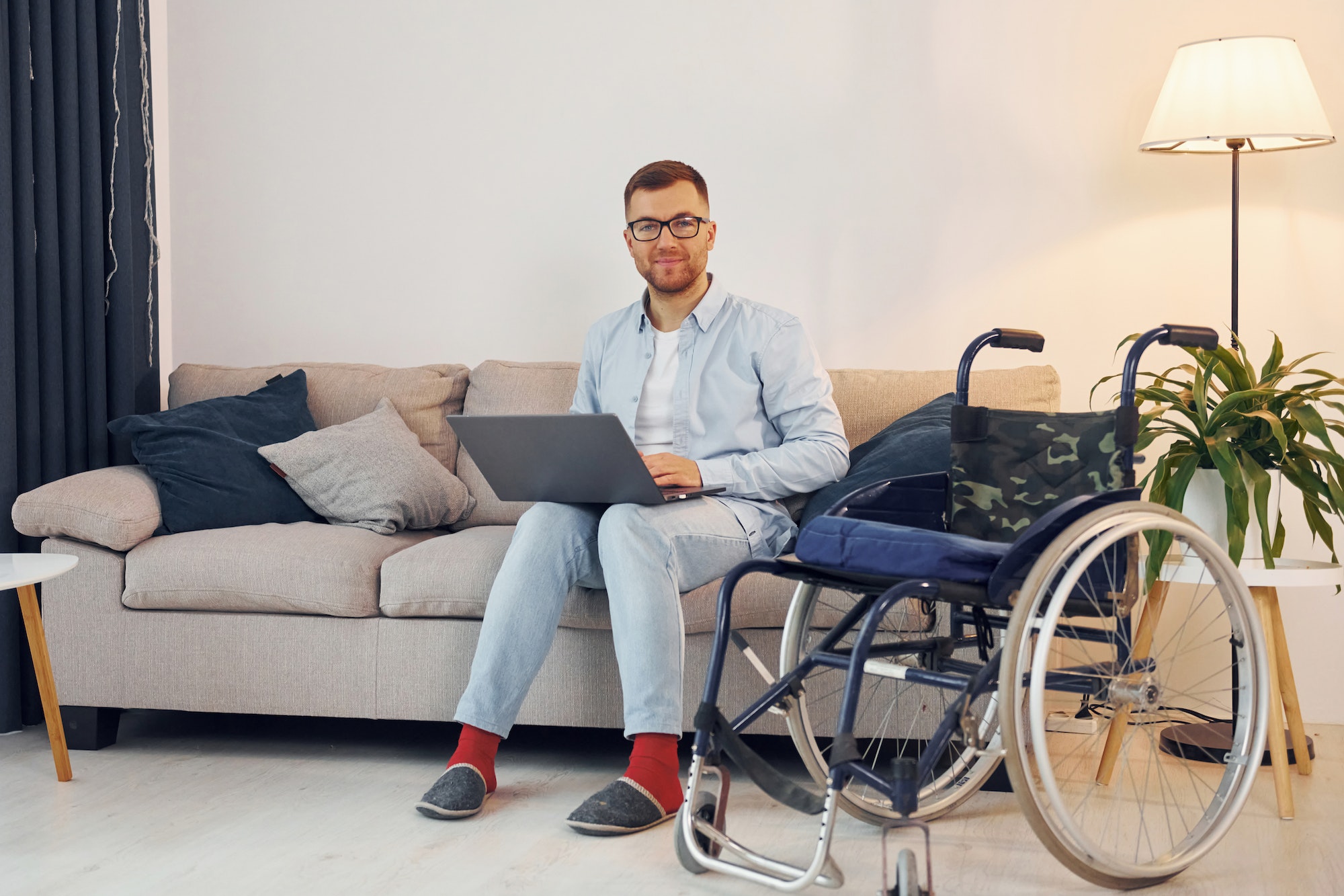With laptop on the legs. Disabled man in wheelchair is at home